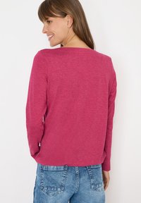 Långärmad topp i en livlig rosa färg med en mjuk textur, med en bred halsringning och subtila detaljer i fållen, matchad med ljusblå denimshorts.