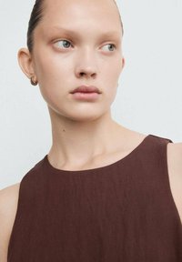 Bruine mouwloze top met een gladde textuur, ronde halslijn en minimalistisch ontwerp, gecombineerd met kleine oorbellen in hoepelvorm.