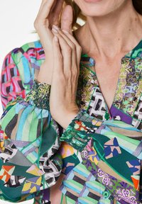Blusa multicolore con tessuto stampato che presenta tonalità di verde, rosa e viola; maniche arricciate; design con bottoni; materiale leggero e testurizzato.