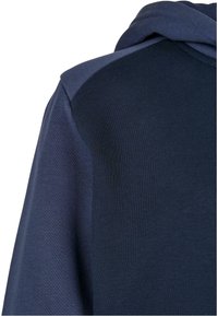 Námořnická modrá mikina s kapucí s jemnou texturou, žebrovanými manžetami a stahovací kapucí. Design obsahuje kontrastní tmavě a světle modré panely.