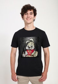 Černé tričko s grafikou karikaturního králíka, který nosí červené tričko s nápisem "THUG FOR LIFE", na šedém texturovaném pozadí.