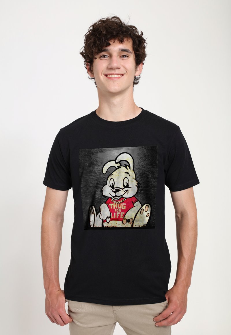 Černé tričko s grafikou karikaturního králíka, který nosí červené tričko s nápisem "THUG FOR LIFE", na šedém texturovaném pozadí.