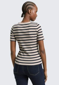 Gestreiftes Kurzarmshirt in Beige und Marineblau, figurbetontes Design, gerippte Textur, Rundhalsausschnitt, kombiniert mit dunklen Denim-Jeans.