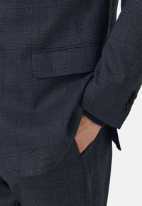 Mörk marinblå kavaj med en subtil rutmönster, strukturerad design och tvåknappslås, sidoficka och textil med textur.