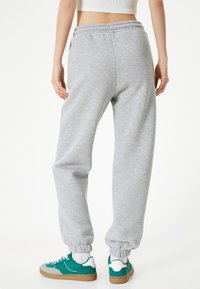 Grijze sweatpants met elastische boorden en tailleband, gemaakt van zachte stof. Draag ze met groen-witte sneakers, gezien vanuit de achterkant.