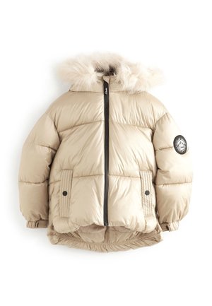 Enfant portant une doudoune beige avec capuche en fourrure, pantalon cargo beige et baskets blanches, debout sur un fond uni.