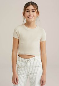 Beige bordázott rövidujjú cropped póló, fehér csíkos nadrággal párosítva, amely gombos záródással és elülső zsebekkel rendelkezik.