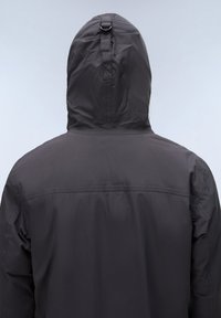 Person mit dunkler, wasserdichter Kapuzenjacke, von hinten vor einem schlichten hellen Hintergrund gezeigt.