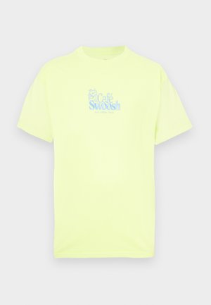 Neónovo žlté bavlnené tričko s krátkymi rukávmi, s modrým vyšívaným logom „Café Swoosh“ na prednej strane. Hladká textúra.