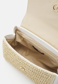 Geweven beige handtas met gestructureerde buitenkant, gouden hardware en een enkele met rits afgesloten binnenzak tegen een lichte stofvoering.