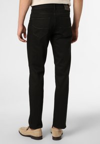 Jeans elásticos negros de corte slim, con bolsillos traseros, costuras sutiles y una textura suave. Combinados con mocasines beiges.