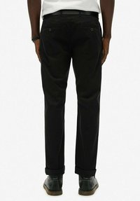 Pantalones negros de tela con un corte recto, que cuentan con puños enrollados, dos bolsillos traseros con cierres de botón y un cinturón.