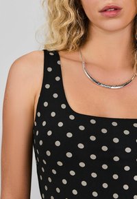 Black tank top with white polka dots, featuring a square neckline and wide straps. Silver necklace sits at collarbone level.