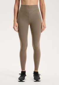 Legginsy treningowe z wysokim stanem w kolorze khaki, o gładkiej fakturze, z trójkątnymi liniami wzorniczymi w pasie oraz dopasowanym krojem.