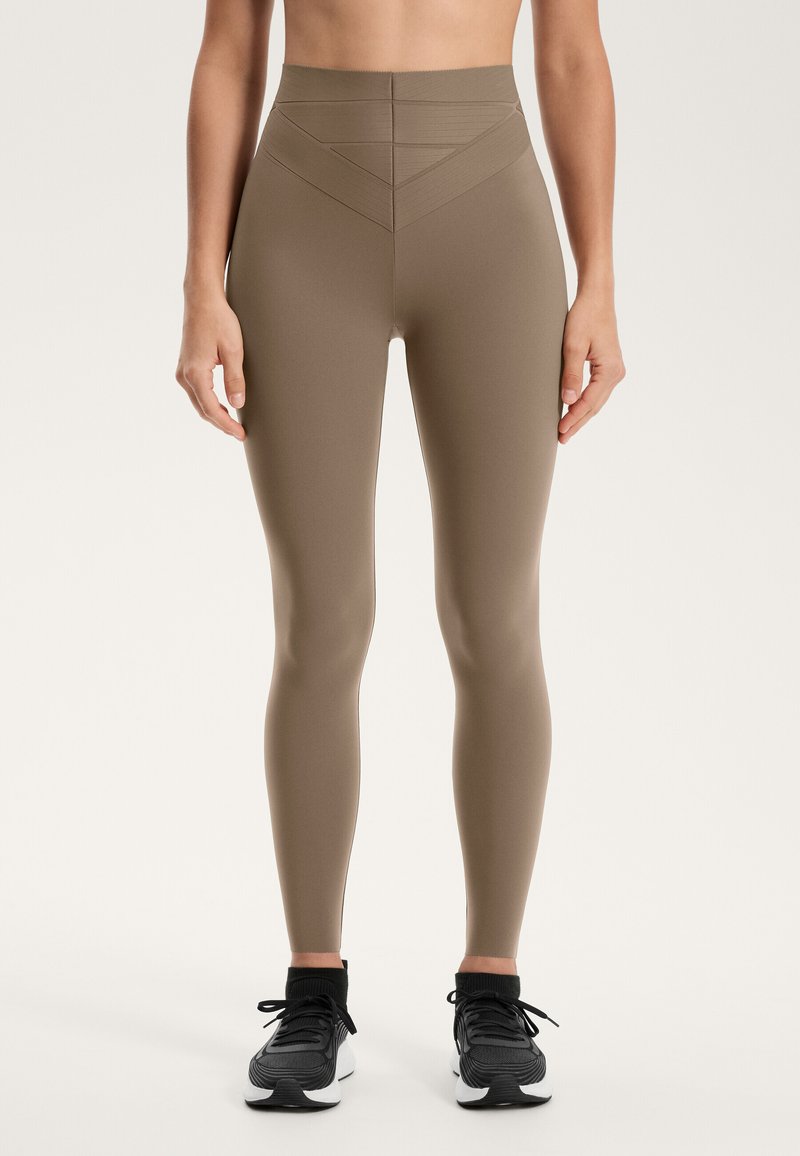 Legginsy treningowe z wysokim stanem w kolorze khaki, o gładkiej fakturze, z trójkątnymi liniami wzorniczymi w pasie oraz dopasowanym krojem.