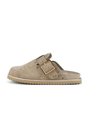 Beige ruskinds slip-on clog med stor firkantet spænde og små dekorative nitter på stroppen, med en rillede gummisål.
