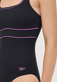 Black one-piece swimsuit with pink trim and small Speedo logo, worn by a person shown from chest to upper thigh.