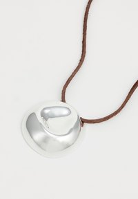 Collana con pendente in argento dalla forma liscia e tondeggiante, attaccata a un cordino in pelle marrone. La superficie riflettente mette in risalto il suo design elegante.