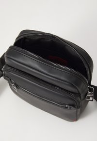 Borsa in pelle nera con vari scomparti con zip, texture liscia e una tracolla corta regolabile. L'interno presenta un'etichetta rossa.