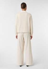 Maglione beige e pantaloni a gamba larga realizzati in un tessuto morbido. Il maglione presenta un colletto rotondo e polsini a coste, mentre i pantaloni hanno un elastico in vita.