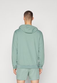 Hoodie verde chiaro con cappuccio regolabile, maniche lunghe e orlo a coste. Texture liscia. Abbinato a pantaloni corti coordinati. Vista posteriore mostrata.
