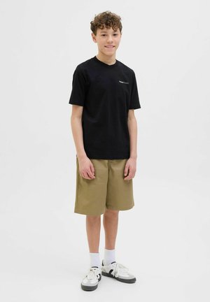 T-shirt en coton noir avec un petit logo, associé à un short en kaki. Le short a une coupe droite et tombe au-dessus du genou. Baskets blanches et noires.