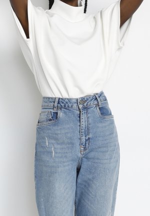Hvid mock-neck top med korte ærmer kombineret med højtaljede, lyseblå, slidte denimjeans. Blødt stof, afslappet pasform og subtil falming.