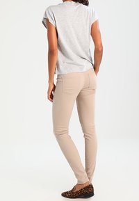Top grigio chiaro a maniche corte, pantaloni beigi aderenti e mocassini maculati marroni. Focus su uno stile casual e un design slim fit.