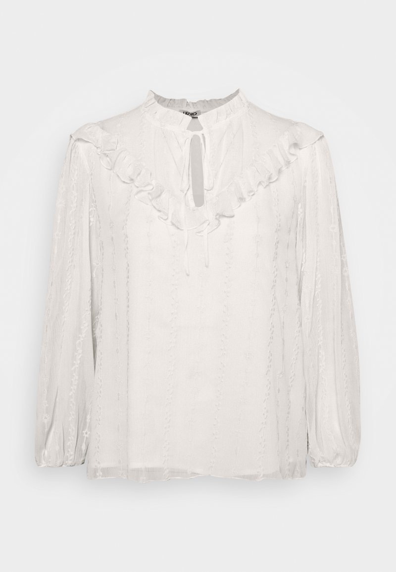 Blouse blanche à manches longues avec col à volants, encolure goutte d’eau avec lien et motifs brodés verticaux subtils.