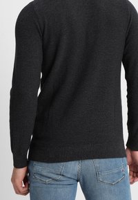 Dunkelgrauer Strickpullover mit strukturierter Oberfläche, Rundhalsausschnitt und gerippten Bündchen. Kombiniert mit hellblauen Jeans, was die Rückansicht zeigt.