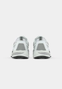 Baskets de sport grises et blanches avec un dessus en mesh, des détails texturés, un talon renforcé et une semelle en caoutchouc noire. Vue arrière, design minimal.