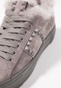 Baskets en daim gris avec de grosses lacets, des clous pyramides gris, un col en fourrure pelucheuse et une semelle en caoutchouc texturée sur fond blanc.