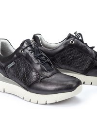 Zapatos de cuero negro con acentos florales texturizados, cordones elásticos y una suela de goma blanca. Punta redondeada y cuello acolchado para mayor comodidad.