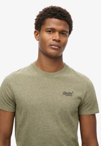 T-shirt in cotone verde con maniche corte, scollo rotondo e tessuto strutturato. Presenta un logo nero sul petto.
