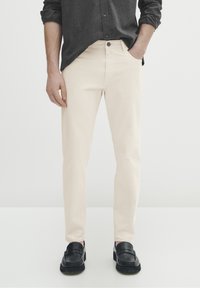 Beiga bomullsbyxor med rak passform, femficksdesign och knäppning fram. Bärs med svarta loafers, vilket visar en slät textur.