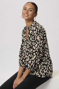 Blusa in stampa leopardata nera e beige con una vestibilità morbida, collo rotondo e maniche arricciate. Il tessuto ha una consistenza liscia.