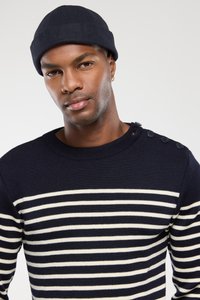 Marineblauer gestreifter Pullover aus Strickstoff. Mit weißen horizontalen Streifen und drei Knöpfen an der Schulter. Begleitet von einer marineblauen Mütze.