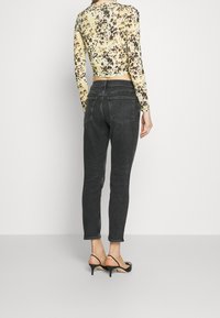 Svarta smala jeans med hög midja och bakfickor, kombinerade med en figurnära långärmad topp med ett gult och brunt blommönster.