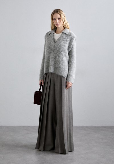 Szürke, bolyhos pulóver, gallérral és V-kivágással, amelyhez magas derekú, bő szárú sötétszürke nadrágot és egy kis barna táskát visel.