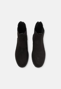 Botas de tobillo de ante negro con una textura suave, paneles laterales elásticos y diseño de punta redondeada. Presenta una suela plana de goma para mayor agarre.