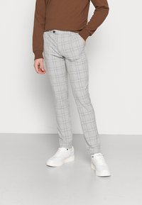 Grå rutig byxor med slim fit, med ett rutmönster i ljusa och mörkare nyanser. Matchas med vita sneakers och en brun topp.