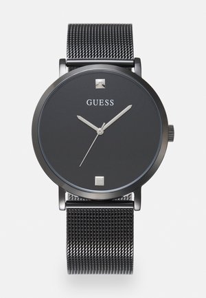 Black Guess wristwatch with silver mesh band, minimalist dial, silver hour, minute, and second hands, and two square markers at 12 and 6 o'clock.
