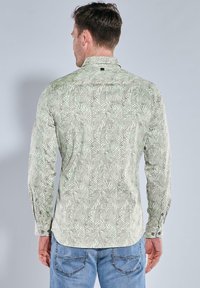 Langärmliges Hemd mit einem grünen und weißen Blattmuster, ausgestattet mit einem Button-Down-Kragen und kontrastierenden Knopfakzenten, aus leichtem Stoff gefertigt.