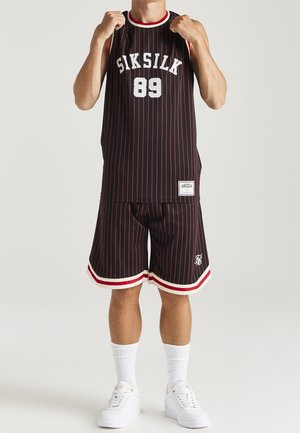 Schwarzes und rotes Basketballtrikot- und Shorts-Set mit weißen Akzenten, Rundhalsausschnitt und Markenlogo-Tag an den Shorts. Die Schuhe sind weiße Sneakers.