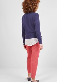 Fioletowa bluza narzucona na białą koszulę w wzory, zestawiona z koralowymi spodniami i granatowymi balerinami. Tkanina o fakturze z prążkowanymi mankietami i dołem.