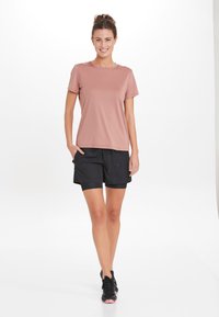 Vaaleanpunainen urheilupaita, jossa on lyhyet hihat, yhdistettynä mustiin shortsihin, joissa on naru. Kangas vaikuttaa sileältä ja hengittävältä.