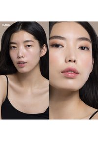 Prodotto trucco "Sand" mostrato su un modello con pelle liscia, top nero e lunghi capelli scuri; presenta un trucco per gli occhi morbido e labbra lucide.