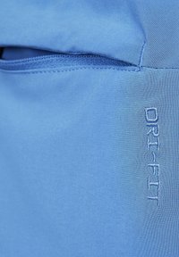 Tissu Dri-FIT bleu clair, texture lisse, avec une petite poche et un détail de logo brodé dans une teinte contrastante.