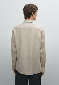 Helle beigefarbene Langarmshirt in entspannter Passform, mit einem einfachen Kragen und geknöpften Manschetten, aus einem glatten, leicht strukturierten Stoff.