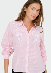 Camicia button-up rosa chiaro con design floreale ricamato bianco, caratterizzata da righe verticali, colletto e maniche lunghe con risvolti.